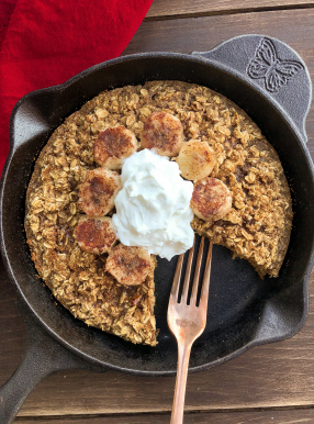 Baked Oatmeal topped with yogurt and bananas in a black skillet.