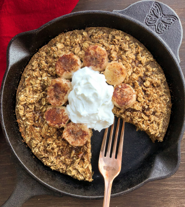 Baked Oatmeal topped with yogurt and bananas in a black skillet.