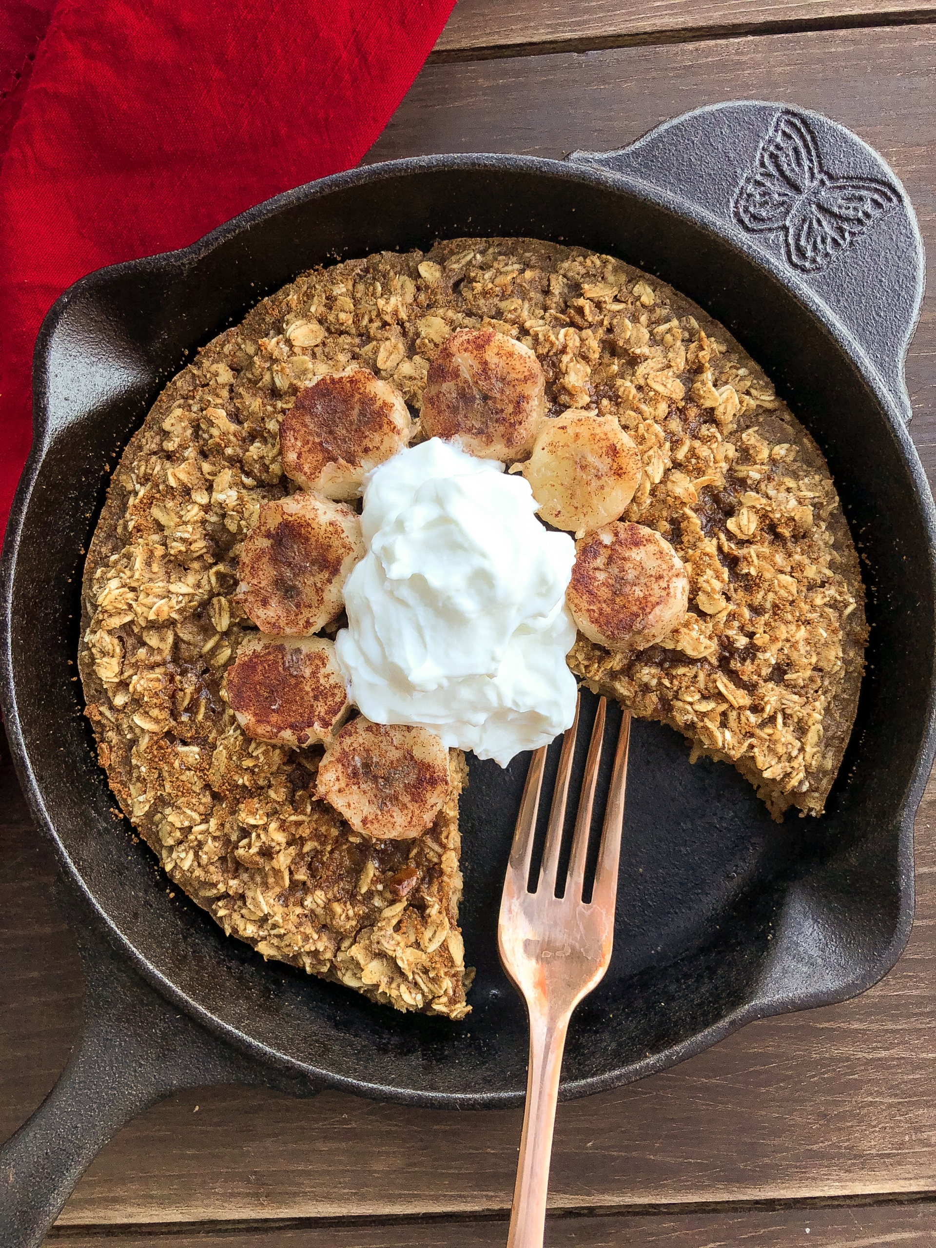 Baked Oatmeal topped with yogurt and bananas in a black skillet.