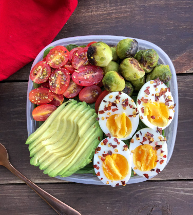 eggs, avocado, tomatoes, and brussel sprouts in a container on a wood piece.