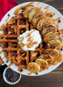 Waffle with bananas, yogurt, peanut butter, and chocolate chips on a white plate.