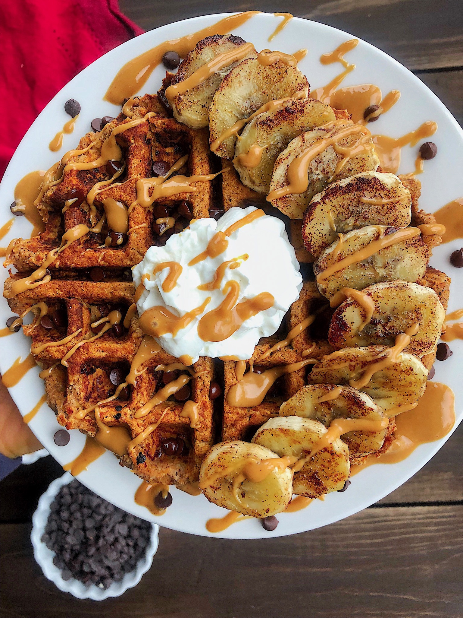 Waffle with bananas, yogurt, peanut butter, and chocolate chips on a white plate.