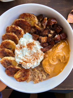 oatmeal with peanut butter, kefir, dates, and bananas on top in a white bowl