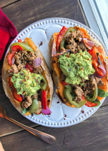 Two sweet potatoes stuffed with beef, peppers, onions, and avocado on a white plate