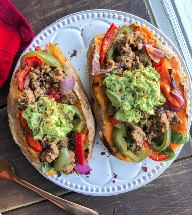 Two sweet potatoes stuffed with beef, peppers, onions, and avocado on a white plate