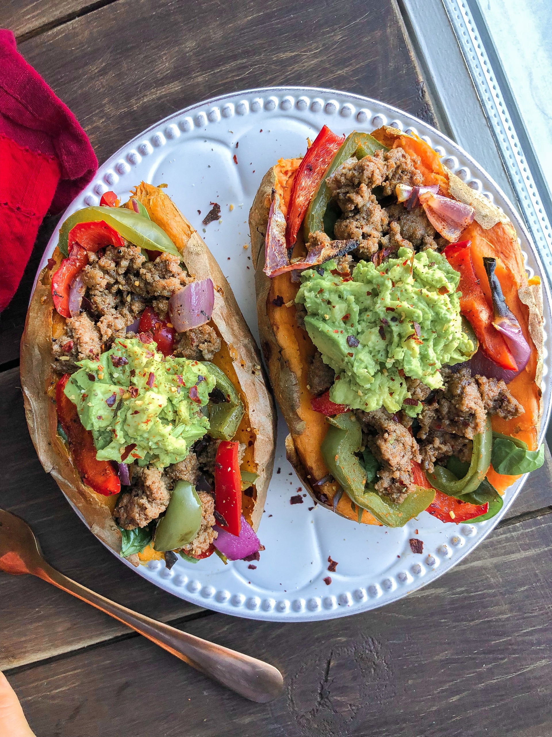 Two sweet potatoes stuffed with beef, peppers, onions, and avocado on a white plate