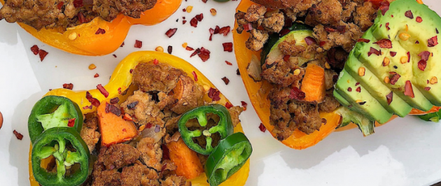 Peppers stuffed with turkey on a white plate with jalapenos, red pepper flakes, and avocado.