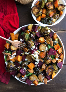 Roasted beet, brussels, sweet potatoes, feta salad in a white bowl on a brown board