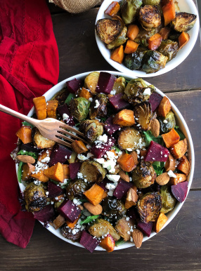 Roasted beet, brussels, sweet potatoes, feta salad in a white bowl on a brown board