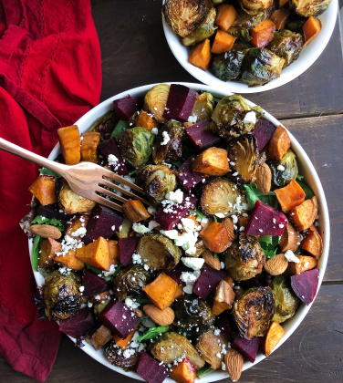 Roasted beet, brussels, sweet potatoes, feta salad in a white bowl on a brown board