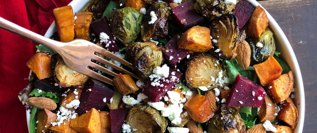 Roasted beet, brussels, sweet potatoes, feta salad in a white bowl on a brown board