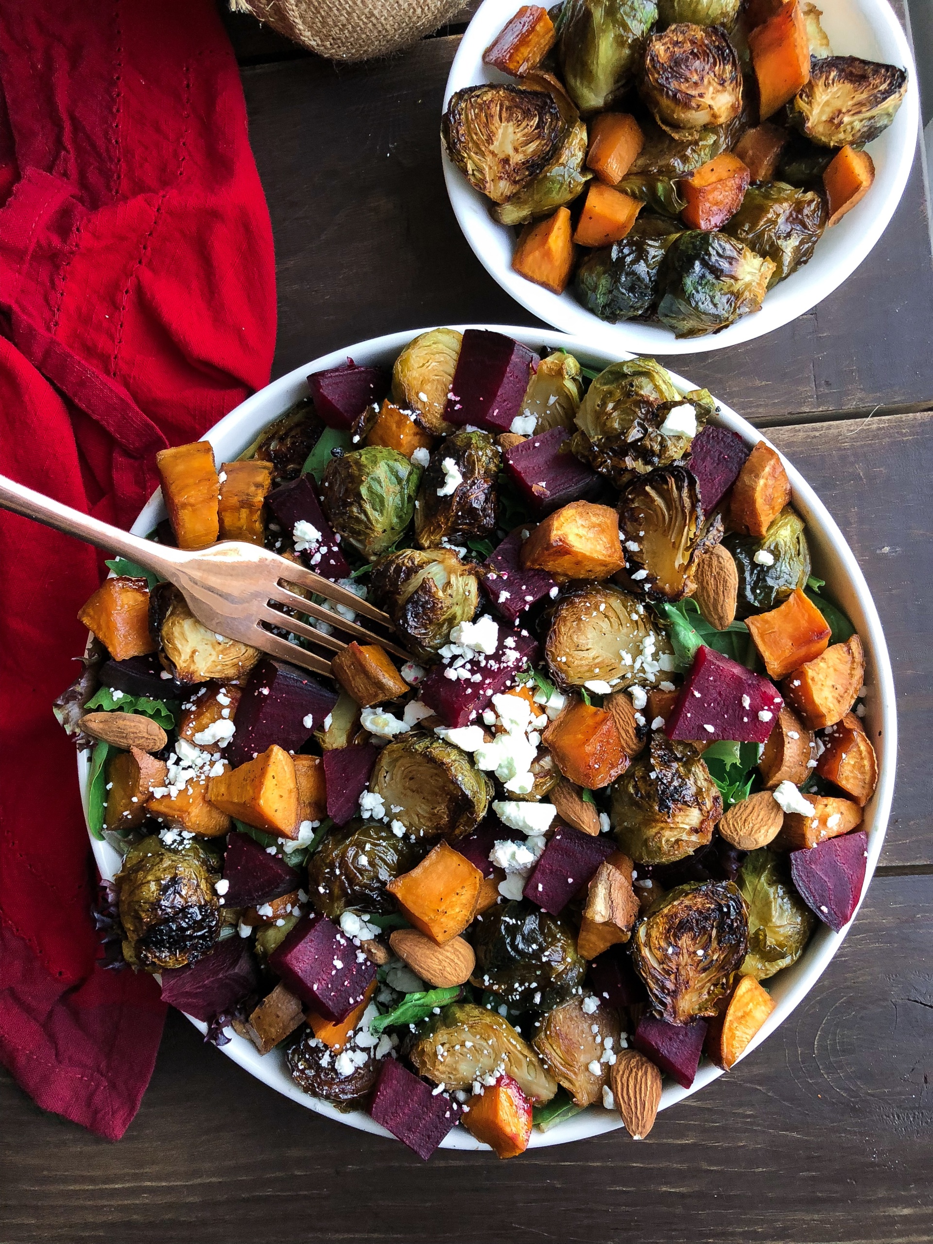 Roasted beet, brussels, sweet potatoes, feta salad in a white bowl on a brown board