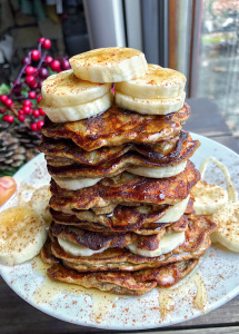 paleo banana pancakes on a white plate with bananas and honey on top.