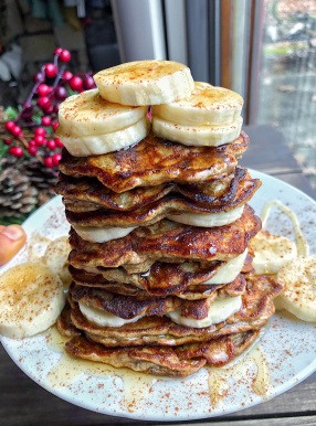 paleo banana pancakes on a white plate with bananas and honey on top.