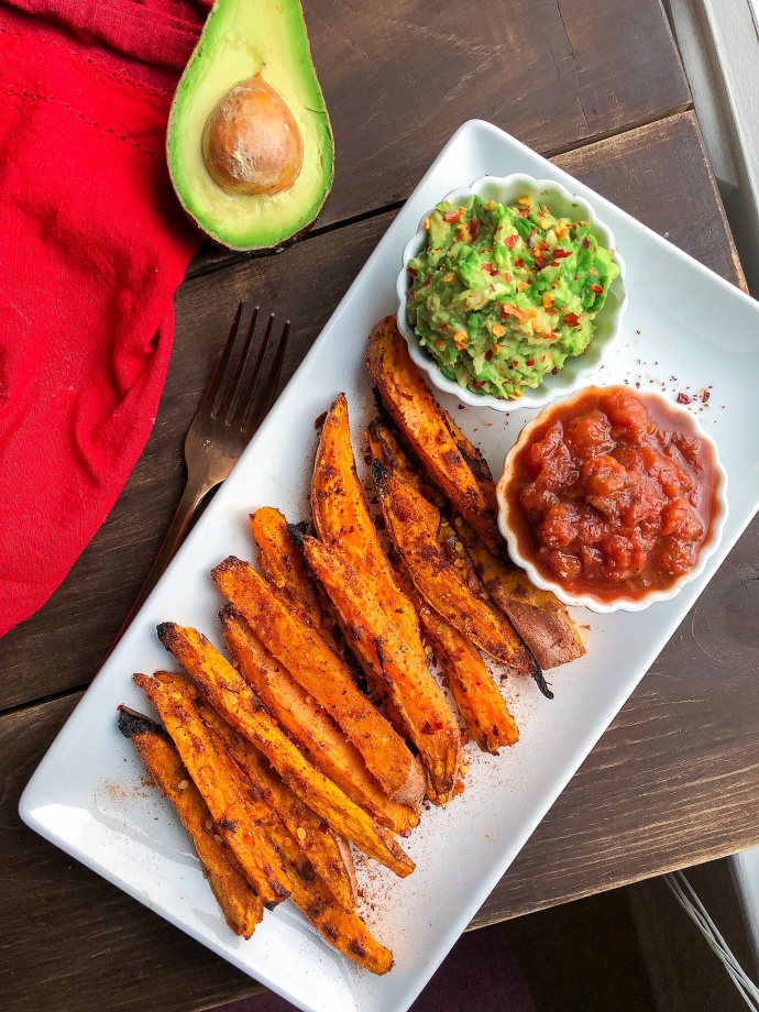 Spicy sweet potato fries on a white plate with salsa and avocado. 