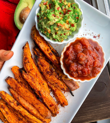 Spicy sweet potato fries on a white plate with salsa and avocado.