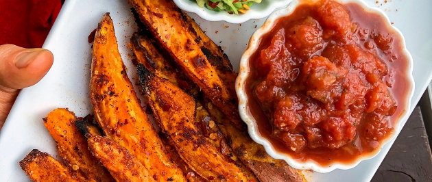 Spicy sweet potato fries on a white plate with salsa and avocado.