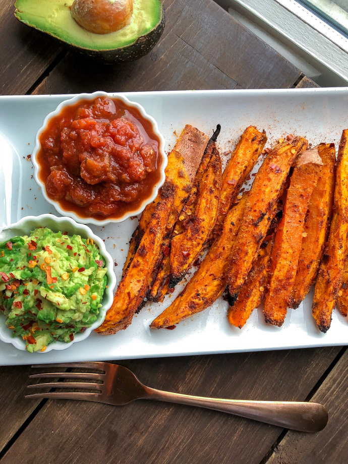 Spicy sweet potato fries on a white plate with salsa and avocado.