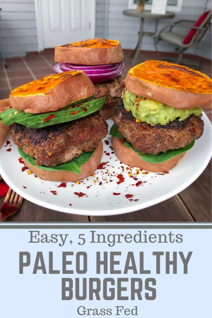 Grass fed burger in between sweet potato buns on a white plate with red pepper flakes.