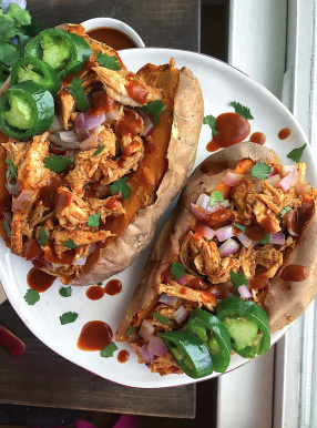 Two sweet potatoes stuffed with bbq chicken on a white plate