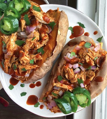 Two sweet potatoes stuffed with bbq chicken on a white plate