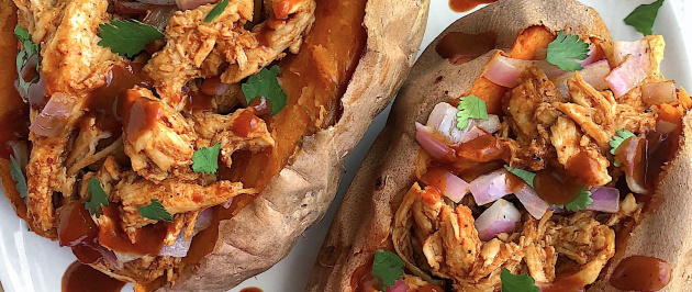 Two sweet potatoes stuffed with bbq chicken on a white plate