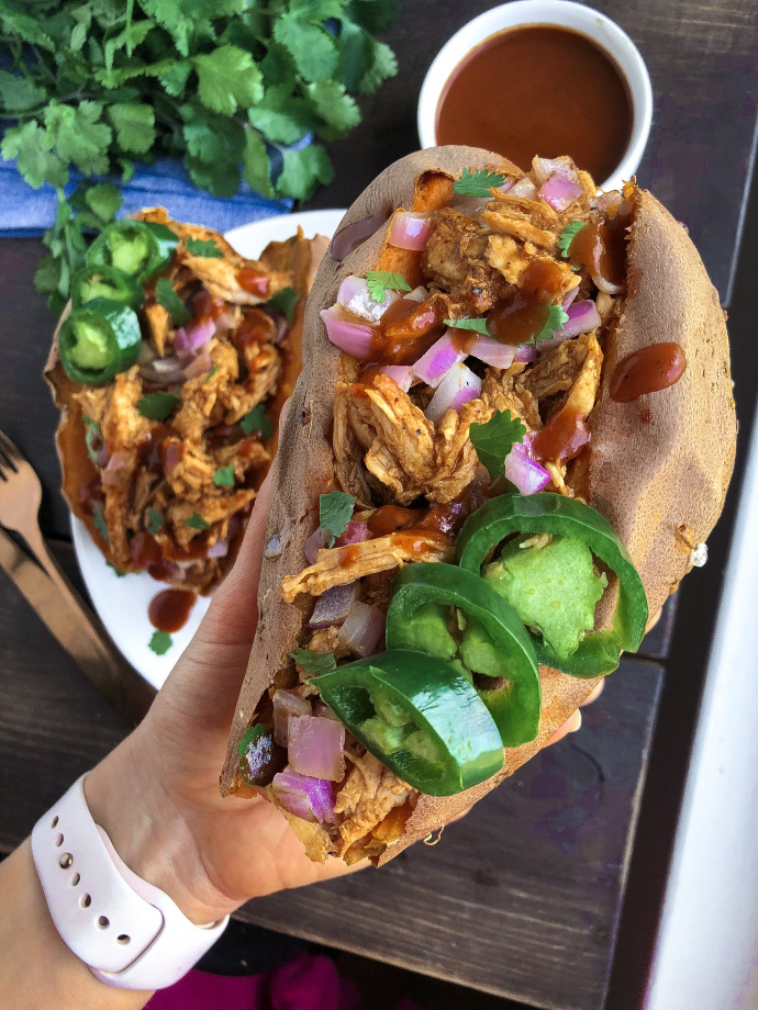 Two sweet potatoes stuffed with bbq chicken on a white plate