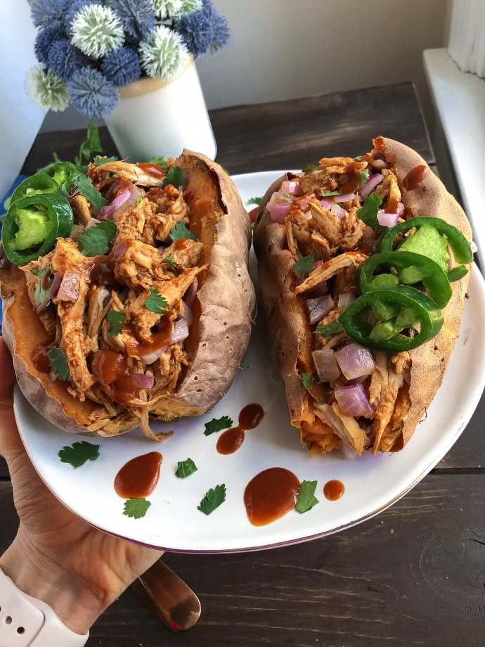 Two sweet potatoes stuffed with bbq chicken on a white plate 