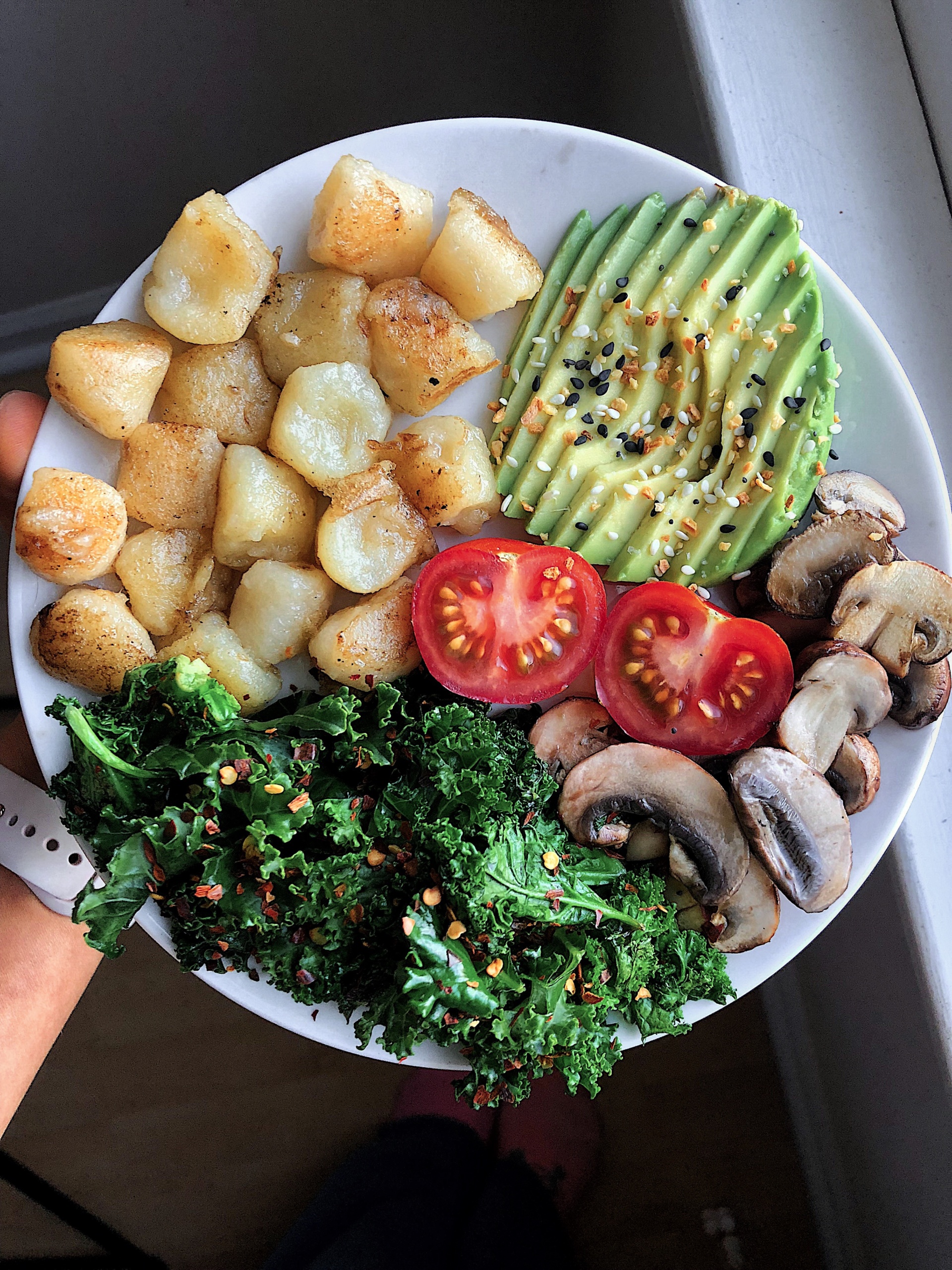 cauliflower gnocchi, avocado, tomato, sautéed mushrooms, and sautéed kale on a white plate