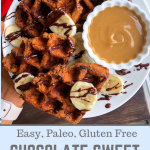 paleo sweet potato waffle on a white plate with cashew butter, bananas, and chocolate drizzled on top