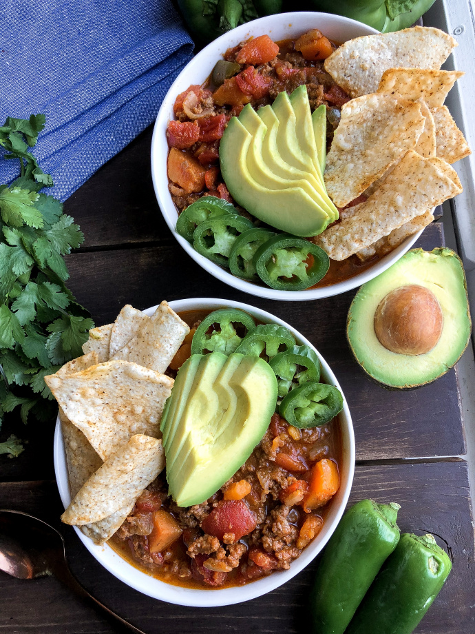 Paleo chili in a bowl with avocado, jalapenos, and tortilla chips in a white bowl. 