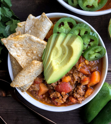 Paleo chili in a bowl with avocado, jalapenos, and tortilla chips in a white bowl.