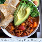 Paleo chili in a bowl with avocado, jalapenos, and tortilla chips in a white bowl.
