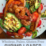 Shrimp, avocado, tomatoes, and spinach stuffed in a sweet potato on a white plate.