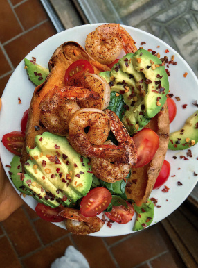 Shrimp, avocado, tomatoes, and spinach stuffed in a sweet potato on a white plate.