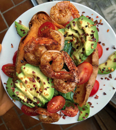 Shrimp, avocado, tomatoes, and spinach stuffed in a sweet potato on a white plate.