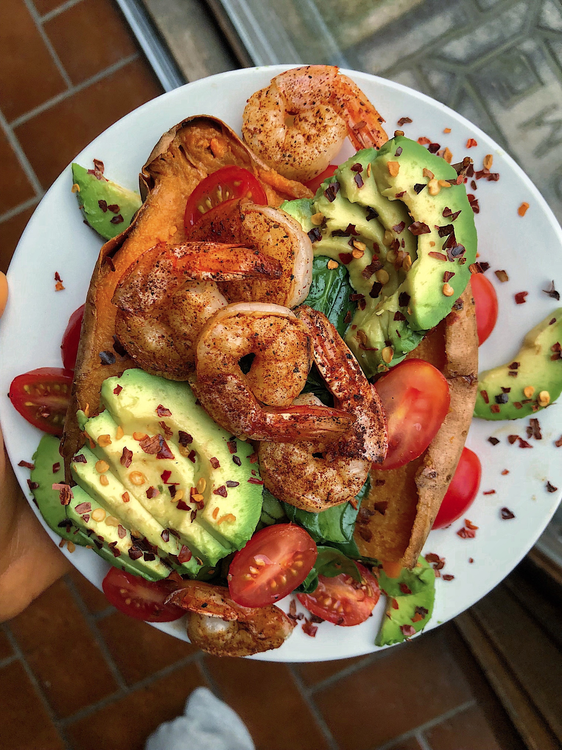 Shrimp, avocado, tomatoes, and spinach stuffed in a sweet potato on a white plate.