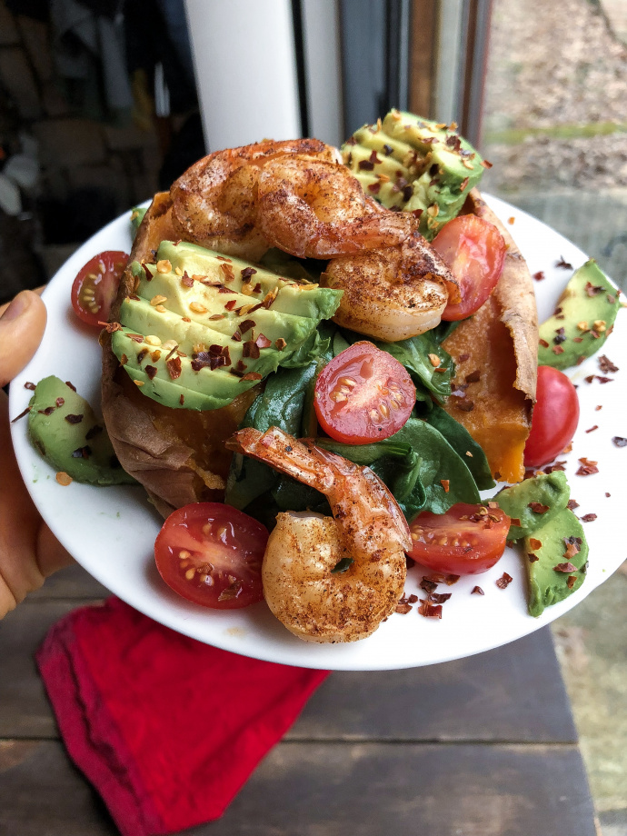 Shrimp, avocado, tomatoes, and spinach stuffed in a sweet potato on a white plate.