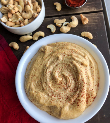 plant based cashew cheese in a white bowl with cashews on a brown board