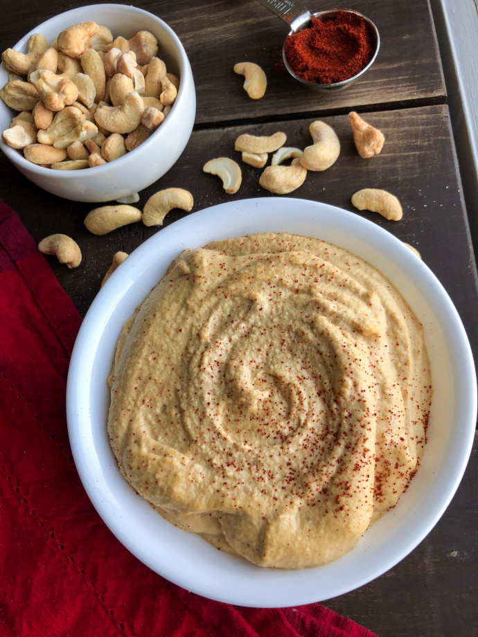 plant based cashew cheese in a white bowl with cashews on a brown board