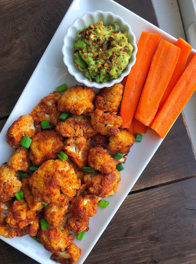 BBQ cauliflower bites on a white plate with carrots and avocado.
