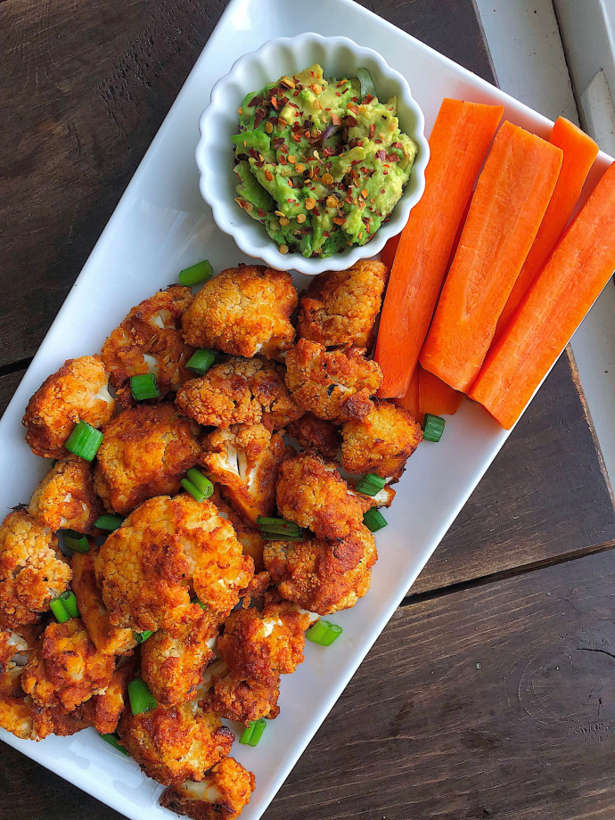 BBQ cauliflower bites on a white plate with carrots and avocado.