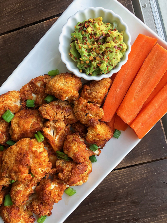 BBQ cauliflower bites on a white plate with carrots and avocado.