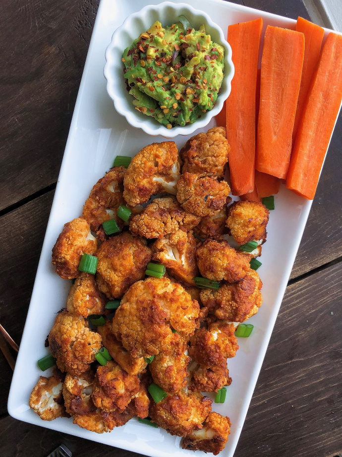 BBQ cauliflower bites on a white plate with carrots and avocado.