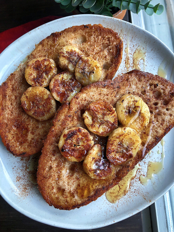 vegan french toast topped with bananas, maple syrup, and cinnamon on a white plate.