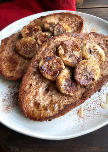 vegan french toast topped with bananas, maple syrup, and cinnamon on a white plate.