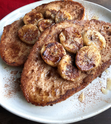 vegan french toast topped with bananas, maple syrup, and cinnamon on a white plate.