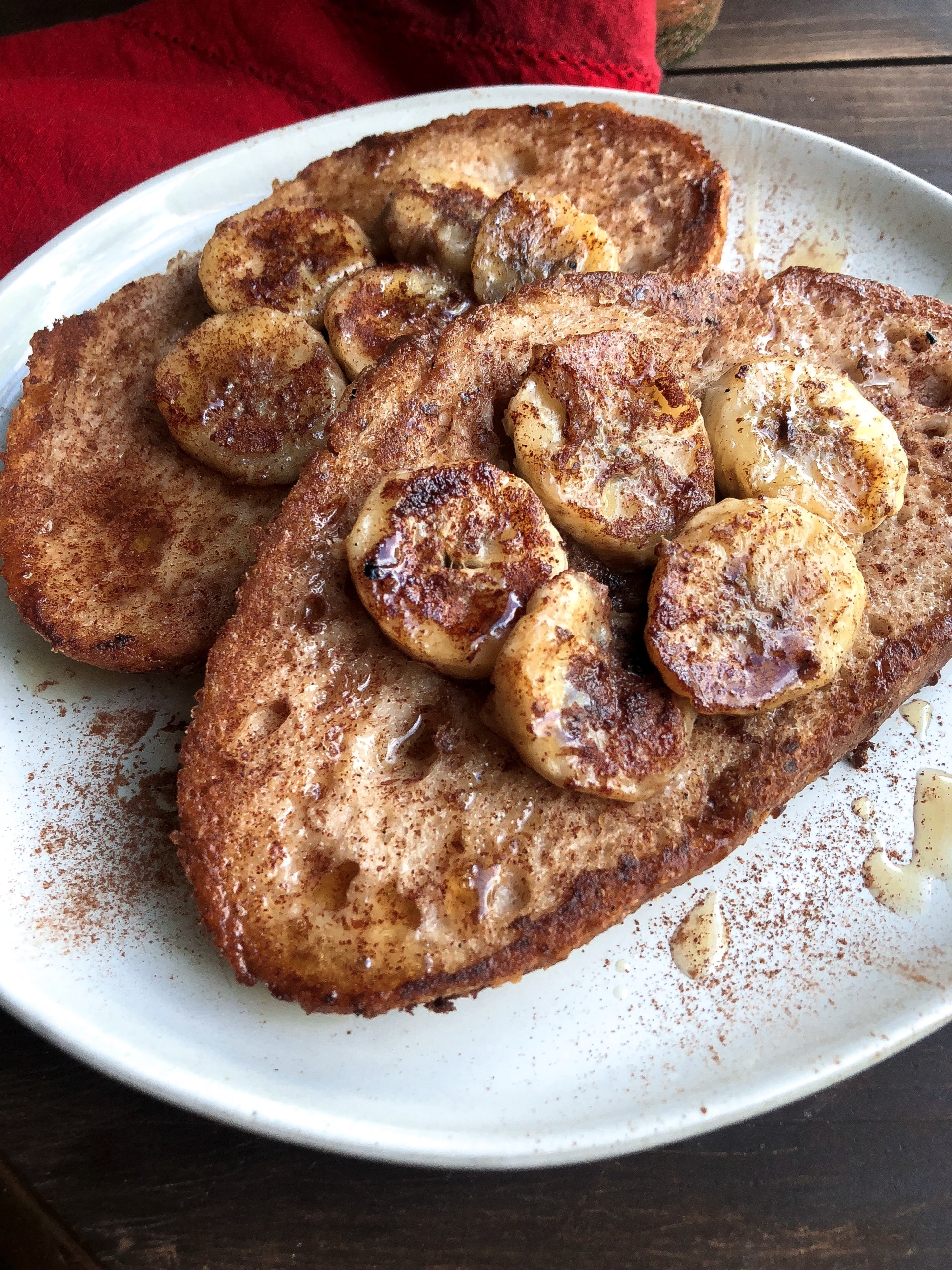 vegan french toast topped with bananas, maple syrup, and cinnamon on a white plate.