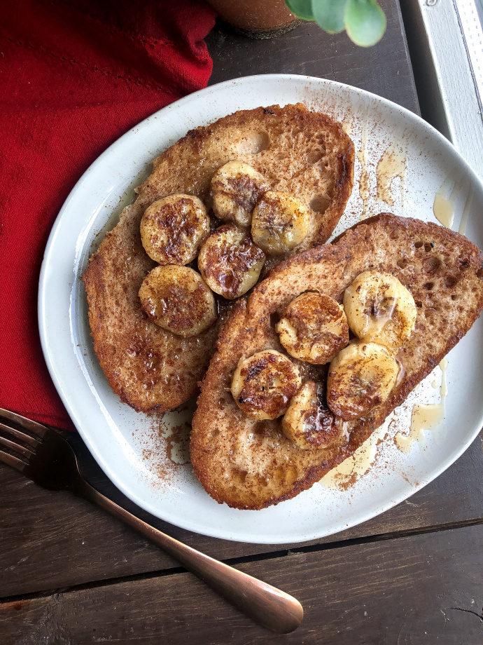 vegan french toast topped with bananas, maple syrup, and cinnamon on a white plate. 