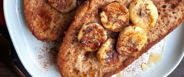 vegan french toast topped with bananas, maple syrup, and cinnamon on a white plate.